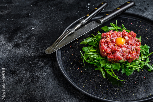 Beef tartare with arugula and quail egg. Black background. Top view. Copy space photo