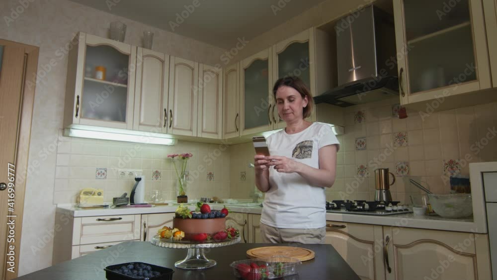Housewife woman finished decorate the chocolate cake with berries and takes photo of it