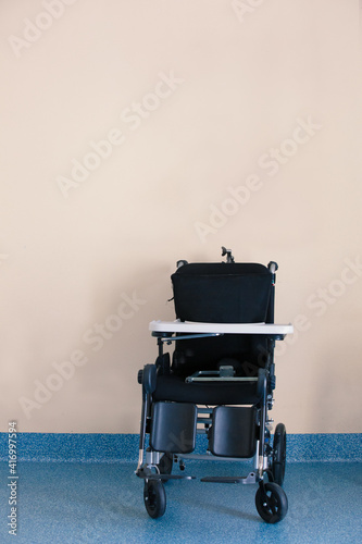 Black Invalid chair for disabled people parked in bright patients living room. Concept of loneliness during the lockdown, soft focus. vertical orientation with copy space for text.