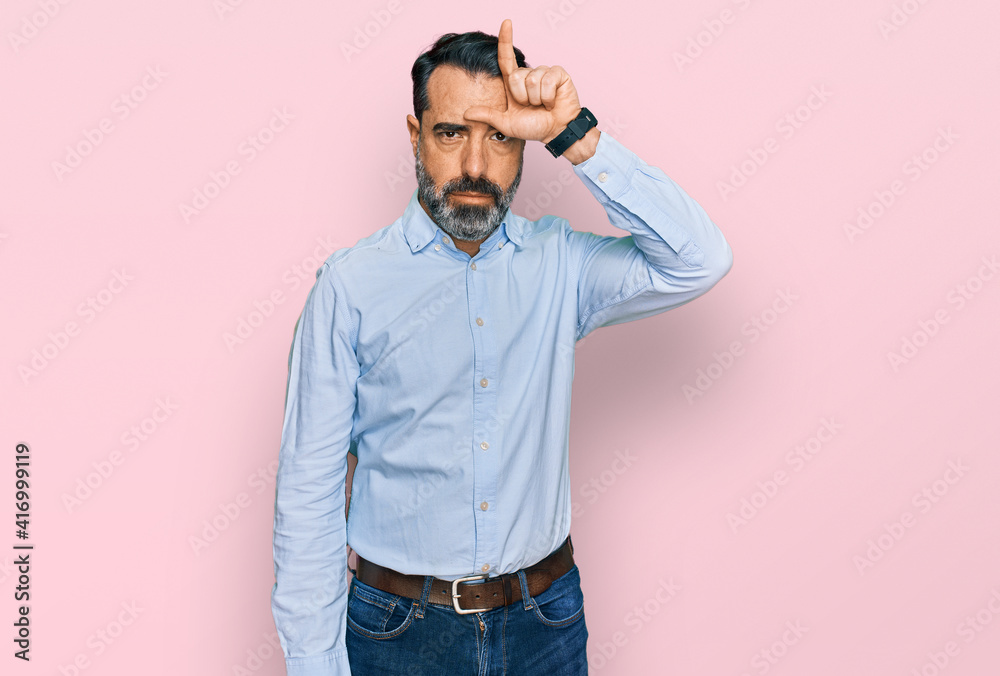Middle aged man with beard wearing business shirt making fun of people with fingers on forehead doing loser gesture mocking and insulting. Middle aged man with beard wearing business shirt making fun of people with fingers on forehead doing loser gesture mocking and insulting.
