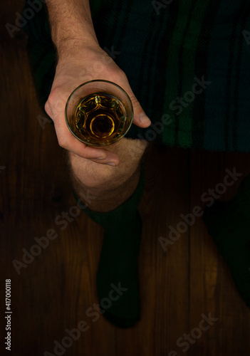 Irish man in traditional green kilt celebrating St. Patrick's Day with scotch drink glass in hand. Scottish guy drinking whiskey in pub minimal style 17 March cultural grand parade celebration Ireland