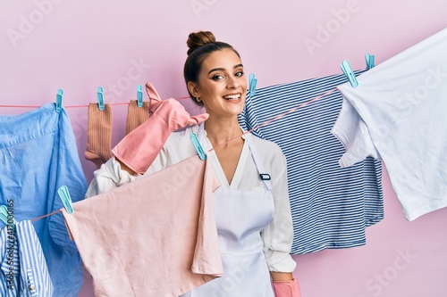 Beautiful brunette young woman washing clothes at clothesline smiling doing phone gesture with hand and fingers like talking on the telephone. communicating concepts.