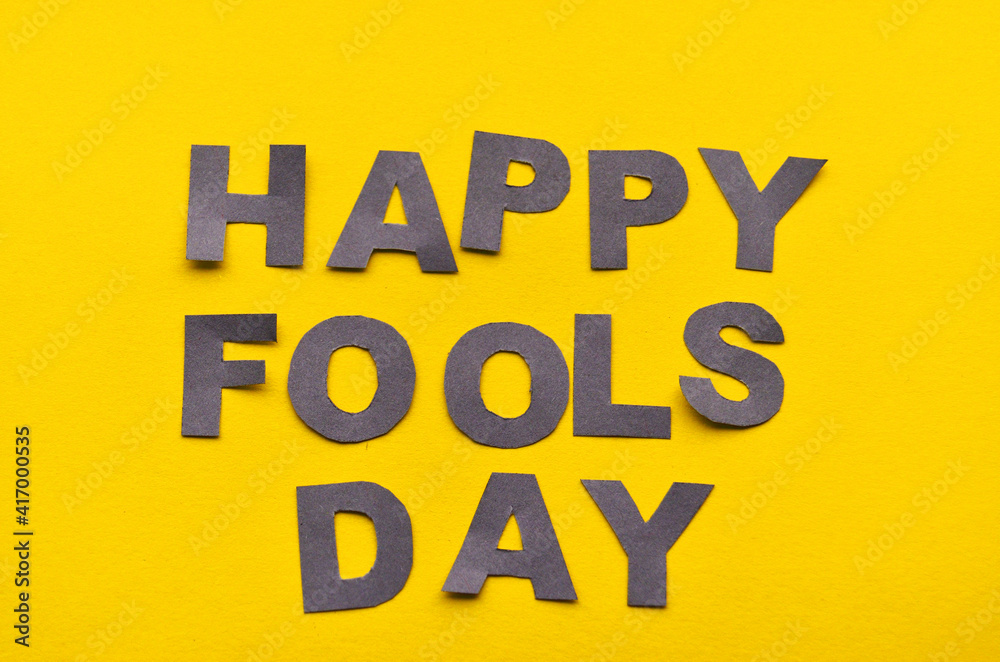 Obraz premium Image caption Happy Fool's Day of grey paper letters on a yellow background close-up. High quality photo