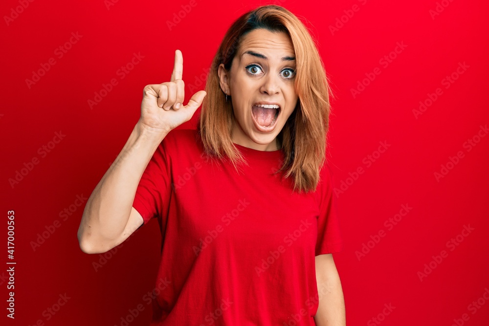 Hispanic young woman wearing casual red t shirt pointing finger up with successful idea. exited and happy. number one. Hispanic young woman wearing casual red t shirt pointing finger up with successful idea. exited and happy. number one.