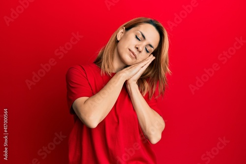 Hispanic young woman wearing casual red t shirt sleeping tired dreaming and posing with hands together while smiling with closed eyes. © Krakenimages.com