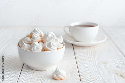 Delicate meringues on a white background with a cup of tea. Side view.