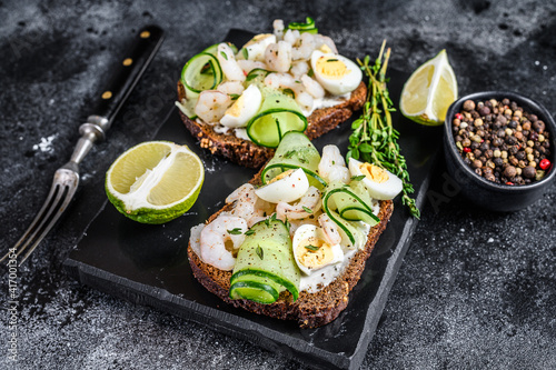 Fresh toasts with shrimp, prawns, quail eggs and cucumber on rye bread. Black background. top view