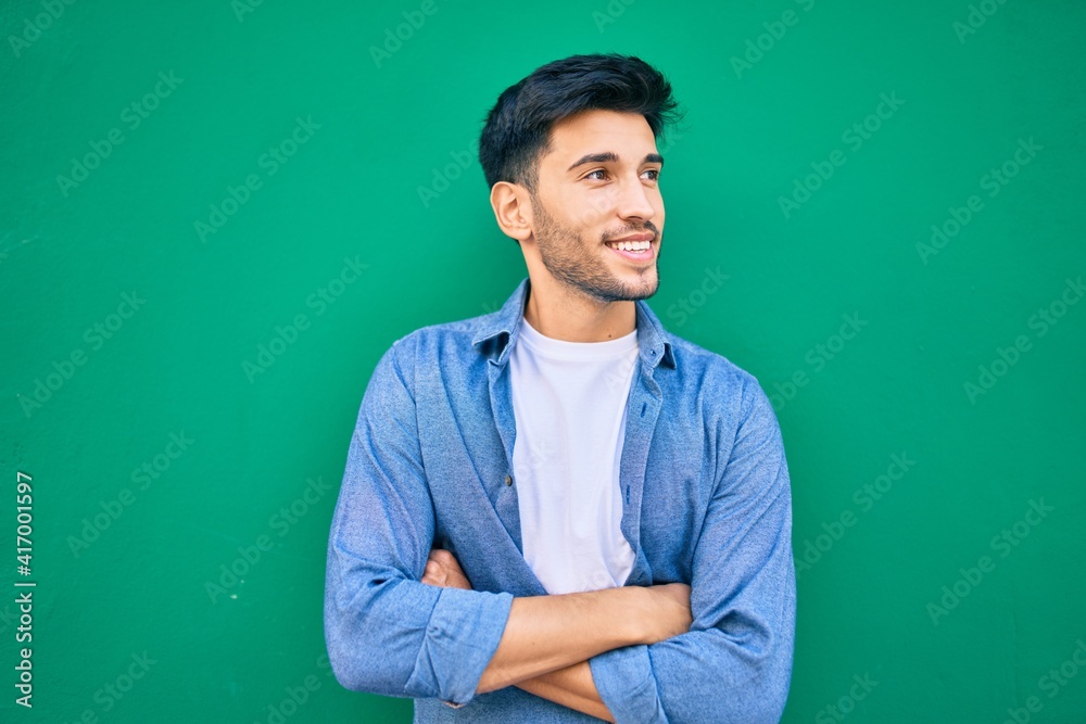 Young latin man smiling happy leaning on the wall at the city. Young latin man smiling happy leaning on the wall at the city.
