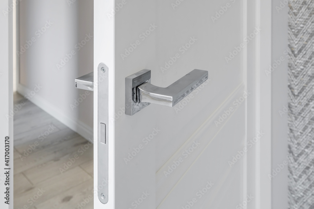 Modern metal door handle on white wooden door in interior. Knob close-up elements. Door handle, fittings for interior design Modern metal door handle on white wooden door in interior. Knob close-up elements. Door handle, fittings for interior design
