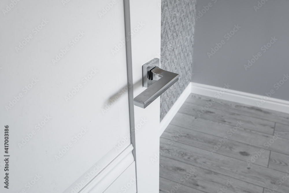 Modern metal door handle on white wooden door in interior. Knob close-up elements. Door handle, fittings for interior design Modern metal door handle on white wooden door in interior. Knob close-up elements. Door handle, fittings for interior design