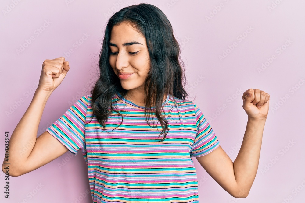 Obraz premium Hispanic teenager girl with dental braces wearing casual clothes showing arms muscles smiling proud. fitness concept.