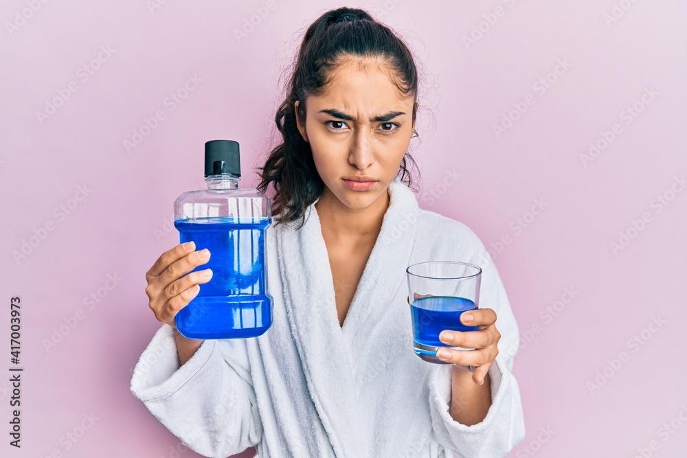 Hispanic teenager girl with dental braces holding mouthwash skeptic and nervous, frowning upset because of problem. negative person. Hispanic teenager girl with dental braces holding mouthwash skeptic and nervous, frowning upset because of problem. negative person.