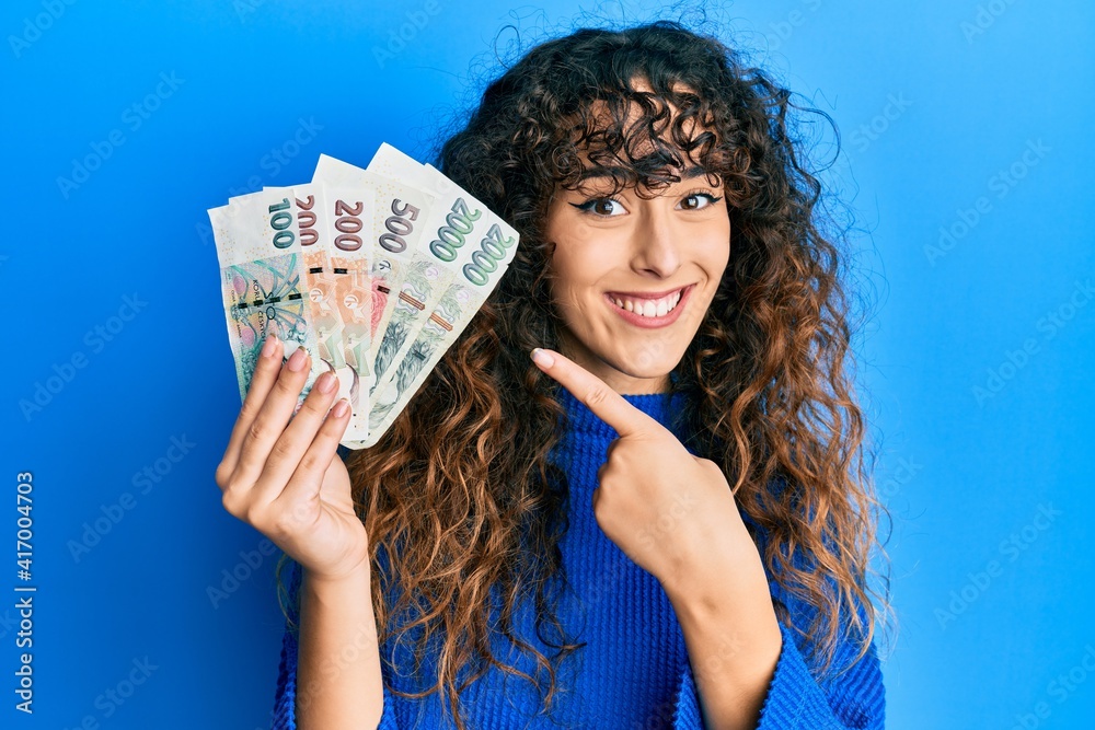 Young hispanic girl holding czech koruna banknotes smiling happy pointing with hand and finger Young hispanic girl holding czech koruna banknotes smiling happy pointing with hand and finger