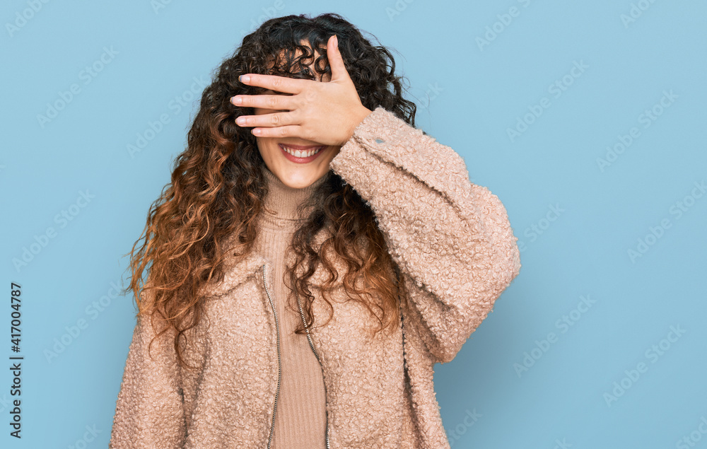 Young hispanic girl wearing winter clothes smiling and laughing with hand on face covering eyes for surprise. blind concept. Young hispanic girl wearing winter clothes smiling and laughing with hand on face covering eyes for surprise. blind concept.