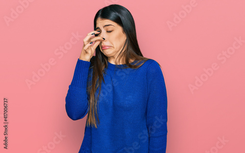 Young hispanic woman wearing casual clothes smelling something stinky and disgusting, intolerable smell, holding breath with fingers on nose. bad smell