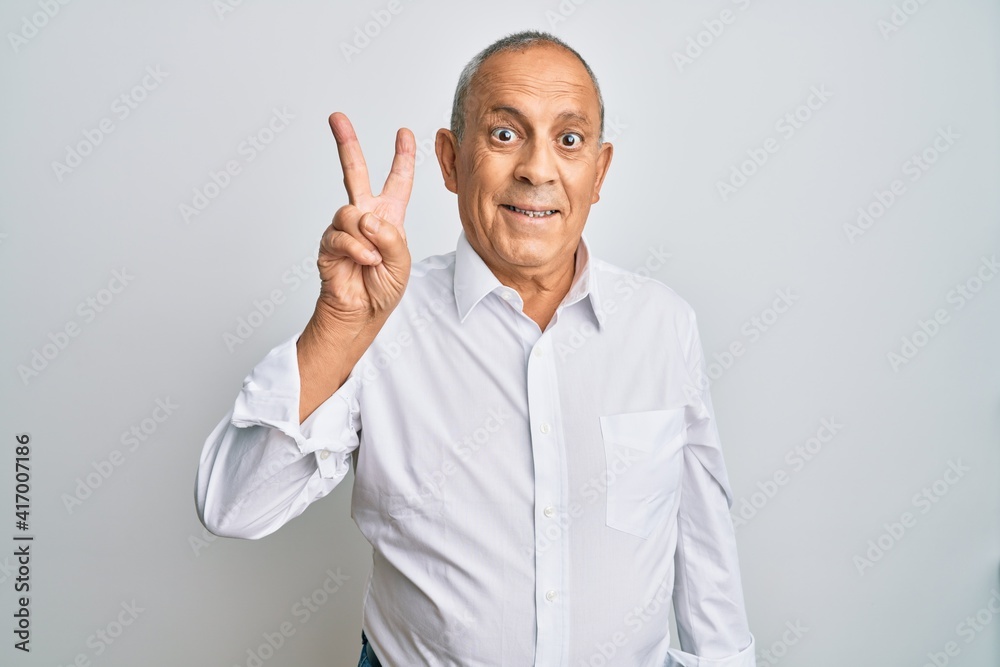 Handsome senior man wearing casual white shirt smiling looking to the camera showing fingers doing victory sign. number two. Handsome senior man wearing casual white shirt smiling looking to the camera showing fingers doing victory sign. number two.