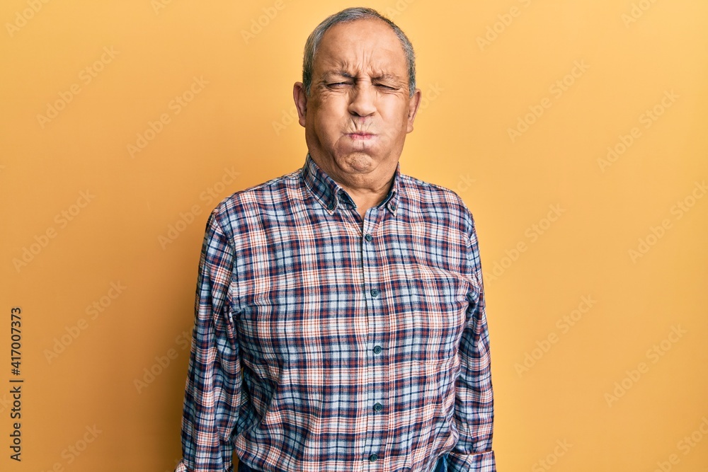 Handsome senior man with grey hair wearing casual shirt puffing cheeks with funny face. mouth inflated with air, crazy expression. Handsome senior man with grey hair wearing casual shirt puffing cheeks with funny face. mouth inflated with air, crazy expression.