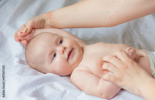 Happy infant girl doing baby massage by his mother at home. Newborn child about 5 months old