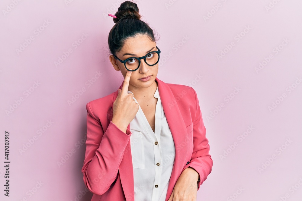 Beautiful middle eastern woman wearing business jacket and glasses pointing to the eye watching you gesture, suspicious expression