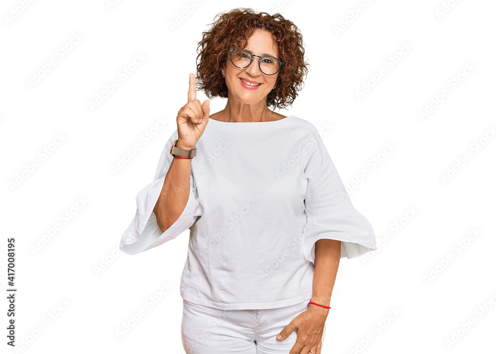 Beautiful middle age mature woman wearing casual clothes and glasses showing and pointing up with finger number one while smiling confident and happy. Beautiful middle age mature woman wearing casual clothes and glasses showing and pointing up with finger number one while smiling confident and happy.