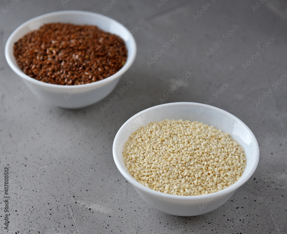 Sesame and flax seed in small white plates on a gray background.