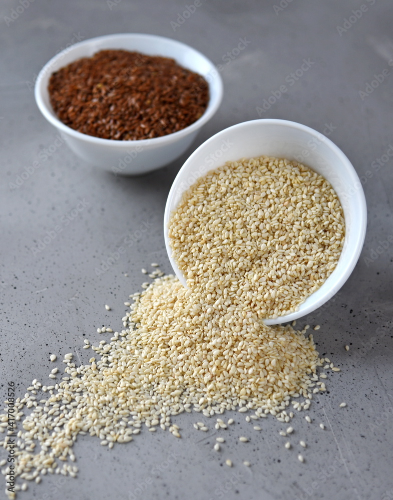 Sesame and flax seed in small white plates on a gray background. Sesame and flax seed in small white plates on a gray background.