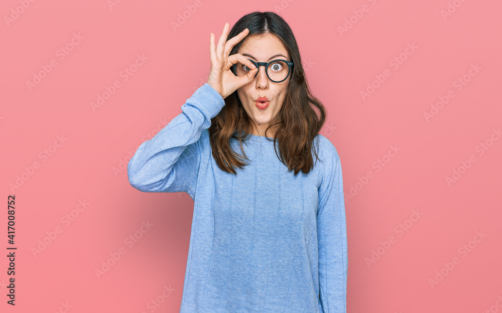 Young beautiful woman wearing casual clothes and glasses doing ok gesture shocked with surprised face, eye looking through fingers. unbelieving expression.