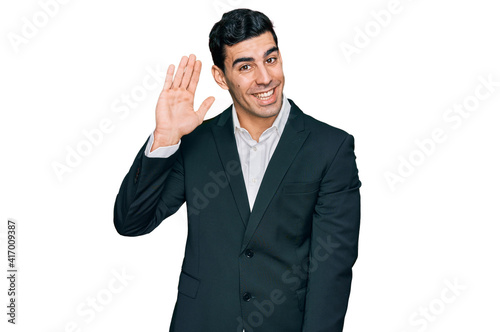 Handsome hispanic man wearing business clothes waiving saying hello happy and smiling, friendly welcome gesture