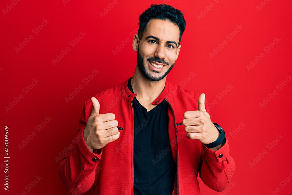 Young hispanic man wearing red leather jacket success sign doing positive gesture with hand, thumbs up smiling and happy. cheerful expression and winner gesture. Young hispanic man wearing red leather jacket success sign doing positive gesture with hand, thumbs up smiling and happy. cheerful expression and winner gesture.