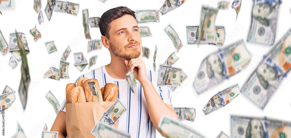 Obraz premium Handsome young man with bear holding paper bag with bread serious face thinking about question with hand on chin, thoughtful about confusing idea