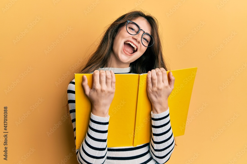 Young caucasian woman reading a book wearing glasses celebrating crazy and amazed for success with open eyes screaming excited. Young caucasian woman reading a book wearing glasses celebrating crazy and amazed for success with open eyes screaming excited.