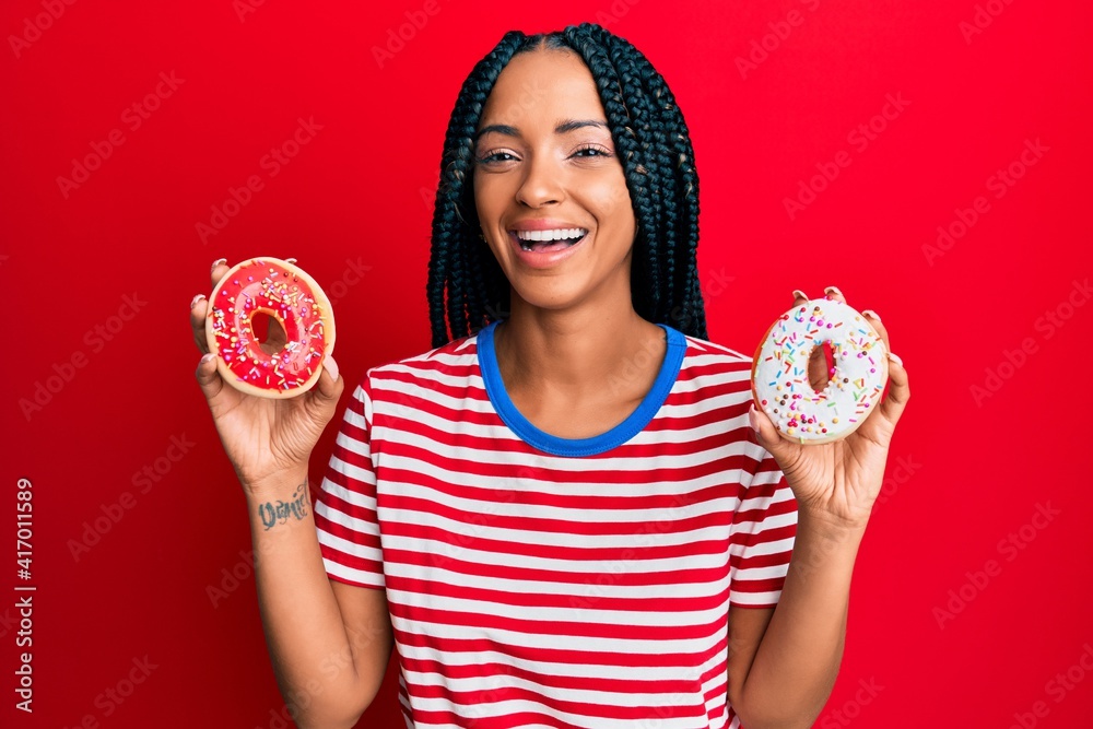 Beautiful hispanic woman holding tasty colorful doughnuts smiling and laughing hard out loud because funny crazy joke. Beautiful hispanic woman holding tasty colorful doughnuts smiling and laughing hard out loud because funny crazy joke.