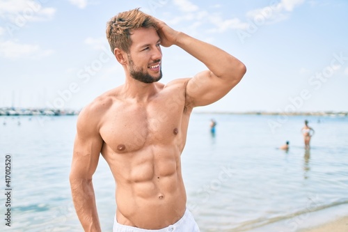 Handsome fitness caucasian man at the beach on a sunny day showing muscular fitness body