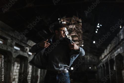 Stylish brutal man in jeans jacket standing in the dark old building and looking to the side