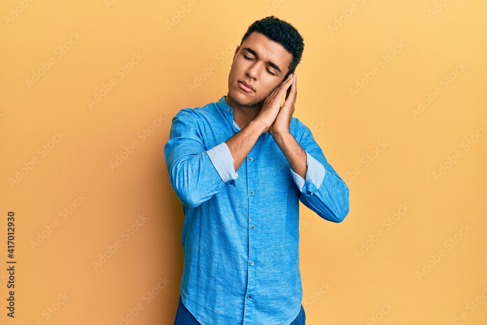 Young arab man wearing casual clothes sleeping tired dreaming and posing with hands together while smiling with closed eyes. Young arab man wearing casual clothes sleeping tired dreaming and posing with hands together while smiling with closed eyes.