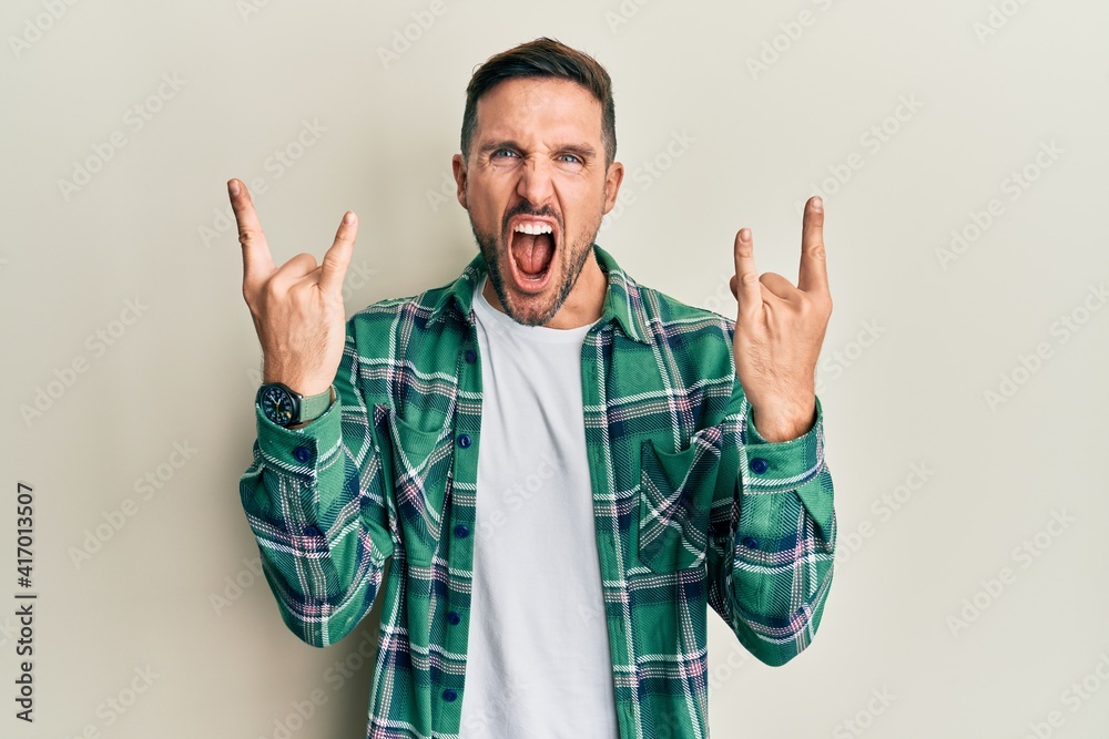 Naklejka premium Handsome man with beard wearing casual clothes shouting with crazy expression doing rock symbol with hands up. music star. heavy concept.