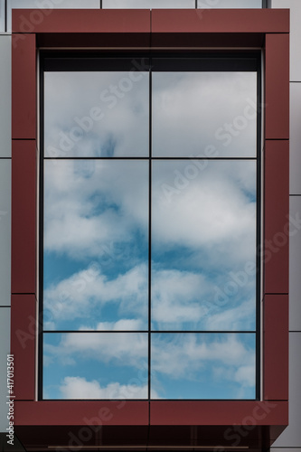 Blue sky and white clouds reflect in a window with red brown frame