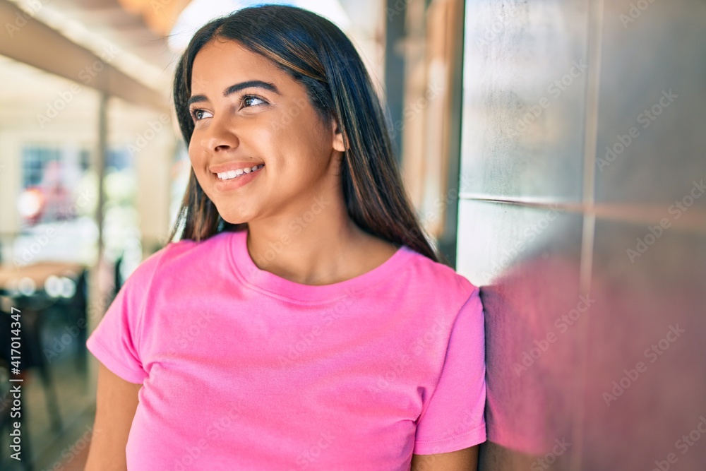 Young latin woman smiling happy leaning on the wall at city.