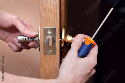 Wallpaper Mural Door installation, worker Installs door knob, woodworker hands close up. A man spins the door handle with a screwdriver, repairs the door handle mechanism Torontodigital.ca