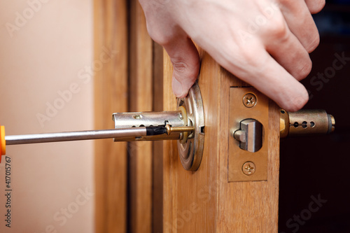 Door installation, worker Installs door knob, woodworker hands close up. A man spins the door handle with a screwdriver, repairs the door handle mechanism