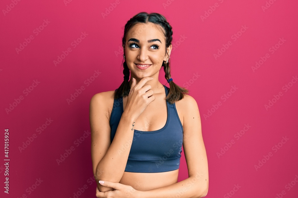 Young brunette girl wearing sportswear and braids with hand on chin thinking about question, pensive expression. smiling with thoughtful face. doubt concept.