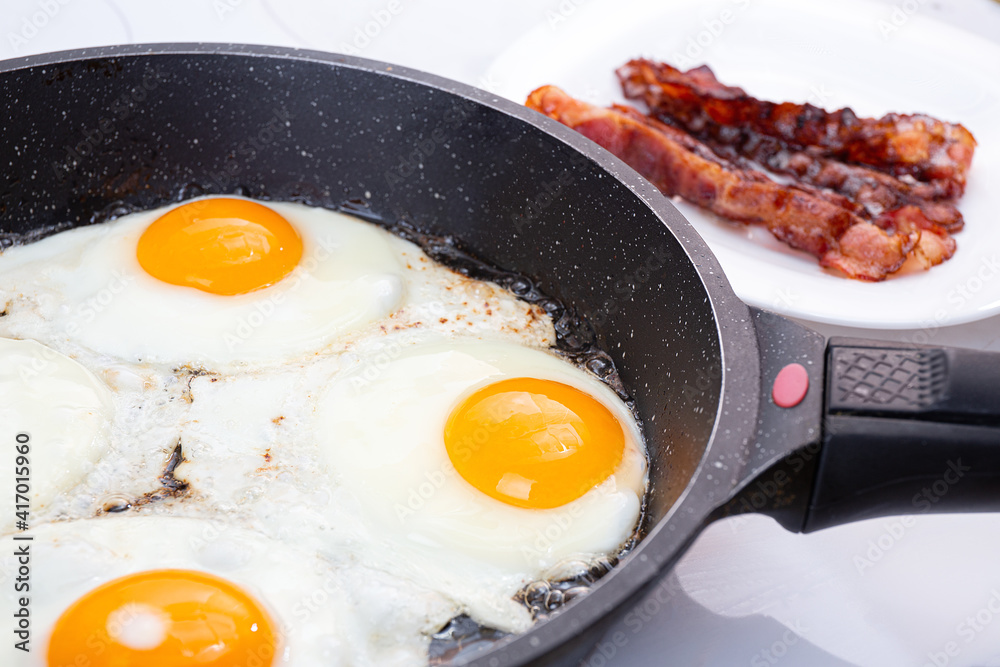 A nutritious breakfast of fried eggs and crispy bacon. The process of cooking a group of eggs in a pan. Crispy bacon on a plate. Idea for a quick, hearty American or British breakfast. A nutritious breakfast of fried eggs and crispy bacon. The process of cooking a group of eggs in a pan. Crispy bacon on a plate. Idea for a quick, hearty American or British breakfast.