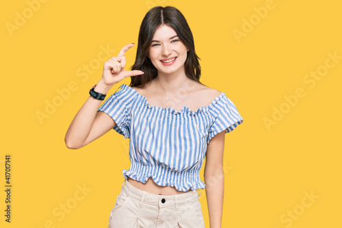 Young beautiful caucasian girl wearing casual clothes smiling and confident gesturing with hand doing small size sign with fingers looking and the camera. measure concept.