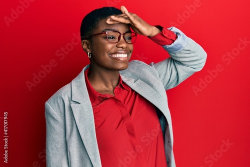 Young african american woman wearing business jacket and glasses very happy and smiling looking far away with hand over head. searching concept.