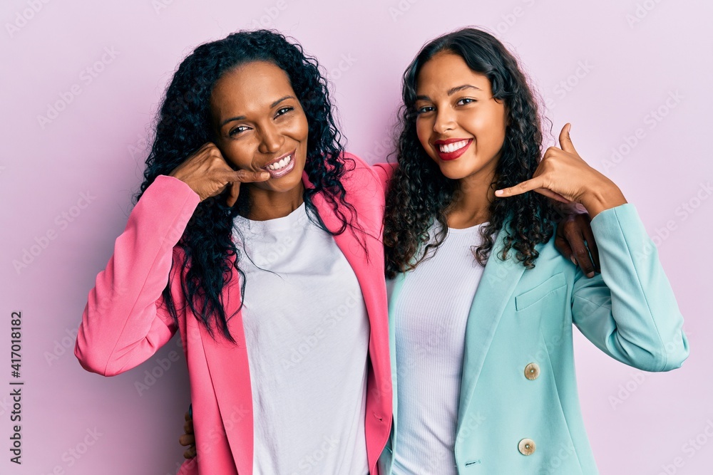 African american mother and daughter wearing business style smiling doing phone gesture with hand and fingers like talking on the telephone. communicating concepts. African american mother and daughter wearing business style smiling doing phone gesture with hand and fingers like talking on the telephone. communicating concepts.
