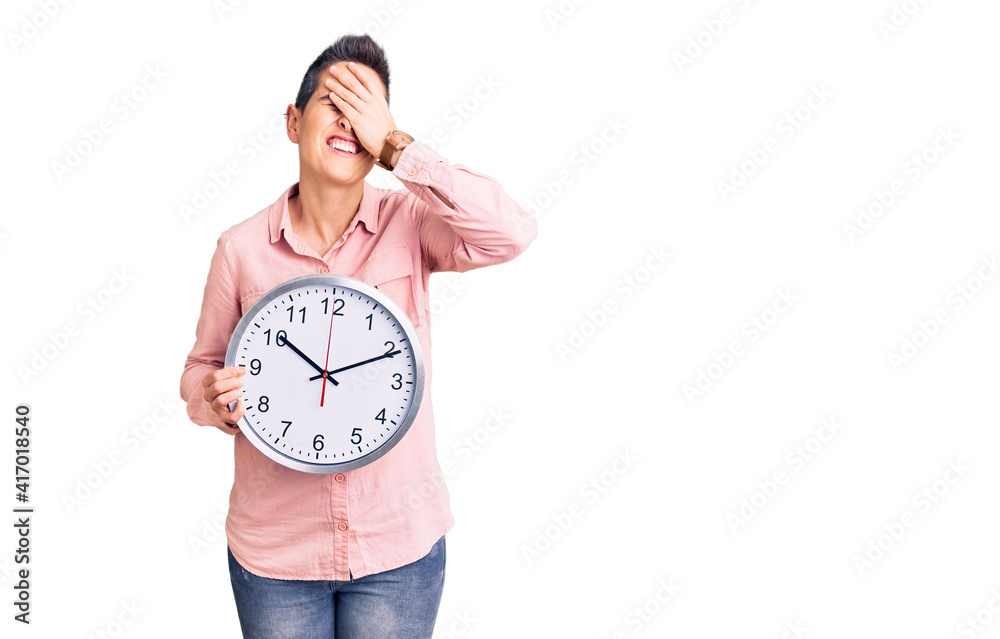 Young woman with short hair holding big clock stressed and frustrated with hand on head, surprised and angry face Young woman with short hair holding big clock stressed and frustrated with hand on head, surprised and angry face