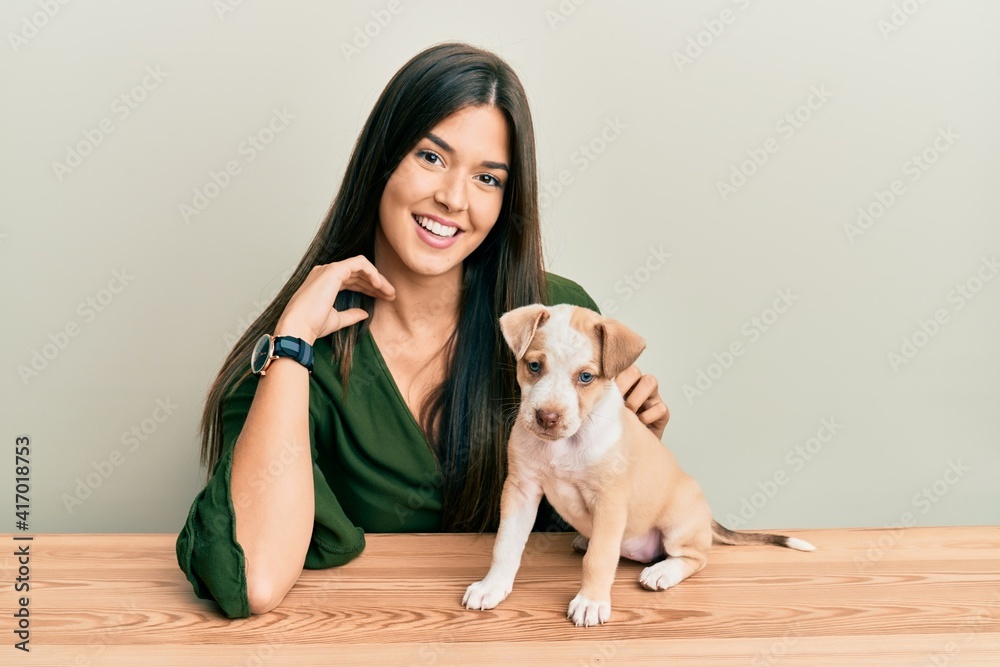 Young hispanic girl smiling happy and playing with dog sitting on the table over isolated white background. Young hispanic girl smiling happy and playing with dog sitting on the table over isolated white background.