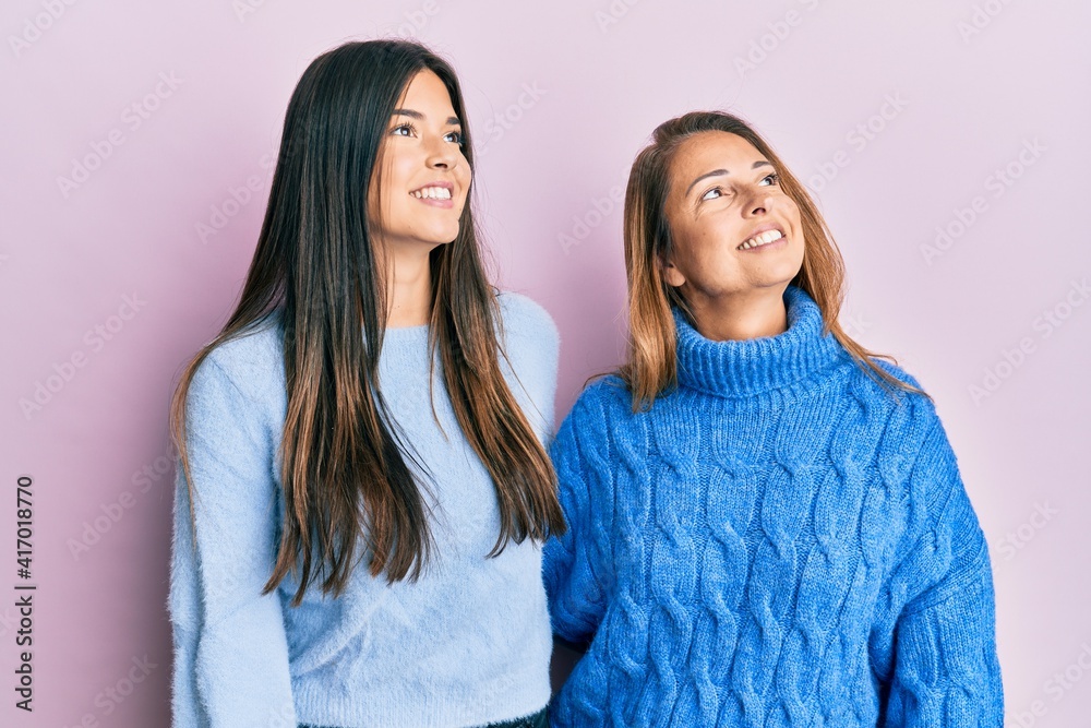 Hispanic family of mother and daughter wearing wool winter sweater looking away to side with smile on face, natural expression. laughing confident. Hispanic family of mother and daughter wearing wool winter sweater looking away to side with smile on face, natural expression. laughing confident.