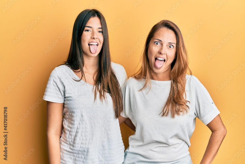 Hispanic family of mother and daughter wearing casual white tshirt sticking tongue out happy with funny expression. emotion concept. Hispanic family of mother and daughter wearing casual white tshirt sticking tongue out happy with funny expression. emotion concept.