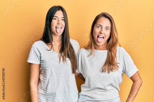 Hispanic family of mother and daughter wearing casual white tshirt sticking tongue out happy with funny expression. emotion concept.